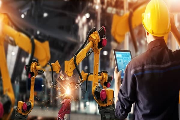 An engineer controlling robotic arm welding on a manufacturing floor