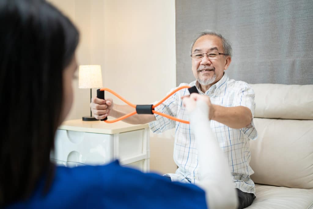 Older handicapped man using resistance stretch band exercise for patient in home nursing care